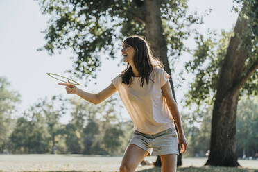 Glückliche reife Frau, die einen Frisbee-Ring wirft, während sie in einem öffentlichen Park an einem sonnigen Tag steht - MFF06410