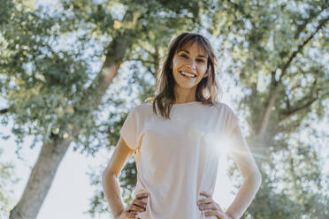 Mature woman with hand on hip standing in public park during sunny day - MFF06412