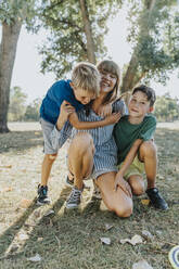 Glückliche Mutter umarmt ihre Söhne in einem öffentlichen Park an einem sonnigen Tag - MFF06415