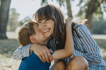 Smiling mother embracing son in public park - MFF06417