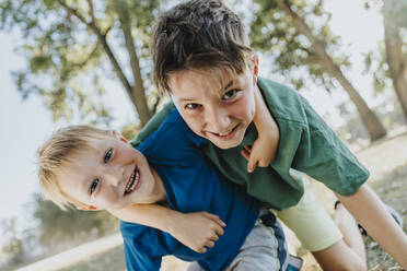 Smiling brothers with arm around kneeling in public park on sunny day - MFF06419