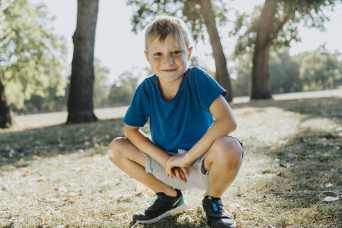Smiling boy crouching in pubic park on sunny day - MFF06422