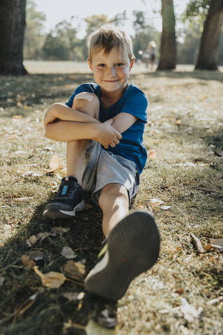 Smiling boy sitting in public park on sunny day stock photo