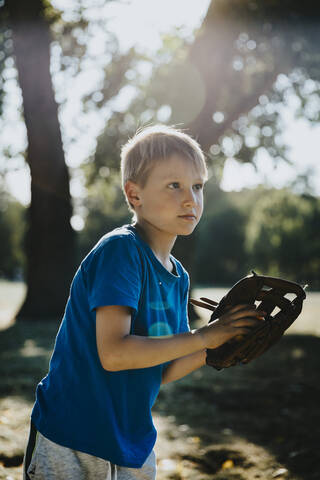 Little boy wearing baseball glove while standing in public park on sunny day stock photo