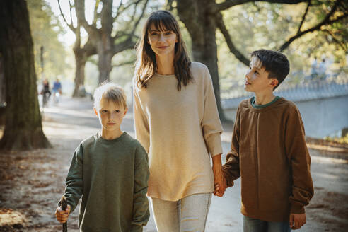 Mother and sons walking in public park on sunny day - MFF06429