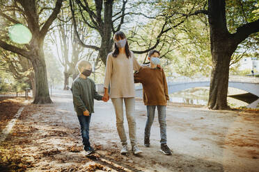 Mutter und Söhne tragen einen Gesichtsschutz beim Spaziergang in einem öffentlichen Park während des Covid-19 - MFF06434