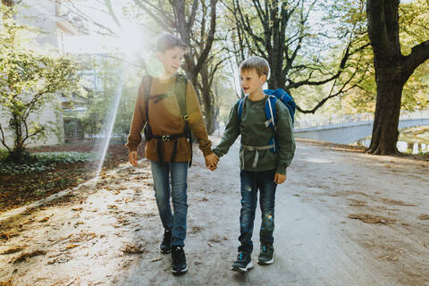 Boy holding hand of younger brother walking in public park on sunny day stock photo