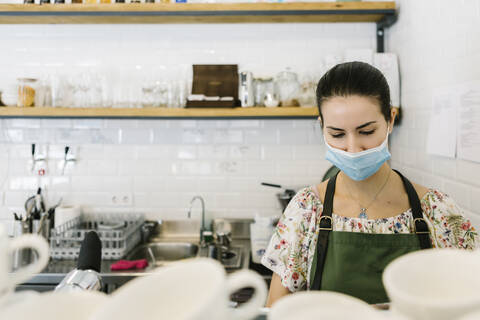 Woman wearing face mask while working in kitchen at coffee shop stock photo