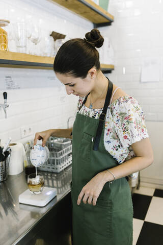 Barista pouring milk in coffee while standing in kitchen at coffee shop stock photo