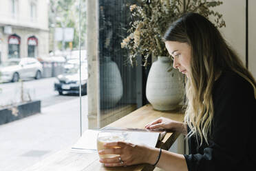 Geschäftsfrau liest eine Zeitschrift und trinkt Kaffee in einem Café - XLGF00603