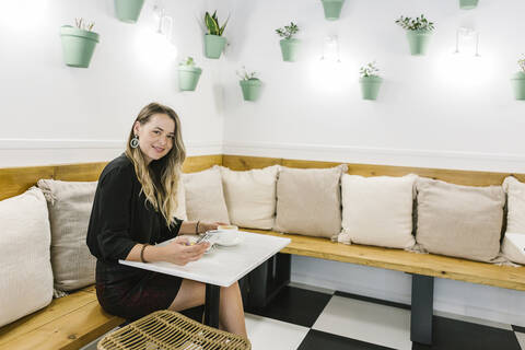 Smiling woman using mobile phone while sitting by table at coffee shop stock photo