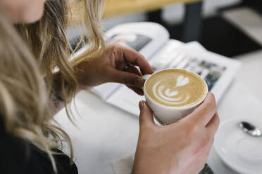 Frau hält Cappuccino-Tasse, während sie in einem Café sitzt - XLGF00609