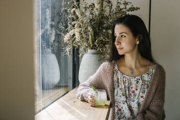 Junge Frau mit Limonadenglas schaut durch das Fenster, während sie in einem Café sitzt - XLGF00613