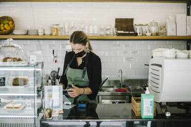 Geschäftsfrau mit Gesichtsmaske, die ein digitales Tablet benutzt, während sie in einem Café steht - XLGF00614