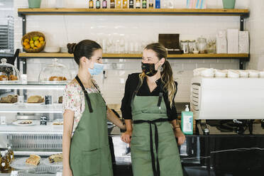 Geschäftsfrauen mit Gesichtsmaske und Schürze stehen an der Theke eines Cafés - XLGF00616