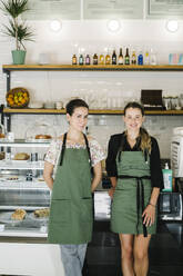 Smiling businesswomen standing by counter at coffee shop - XLGF00619