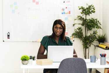 Businesswoman using laptop while sitting by desk at office - GIOF09234