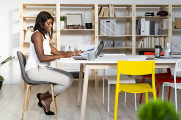 Businesswoman working while sitting by table at office - GIOF09275