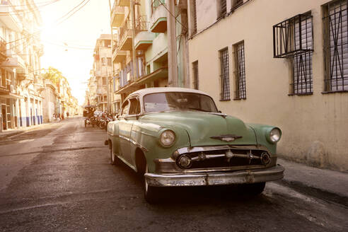 Cuba, La Habana Province, Havana, Pastel green vintage car parked along city street at sunset - RNF01297