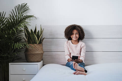 Cute girl using smart phone sitting in bedroom at home stock photo