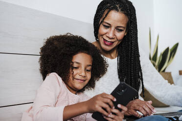 Tochter text messaging auf Smartphone mit Mutter auf Bett im Schlafzimmer zu Hause - EBBF00933