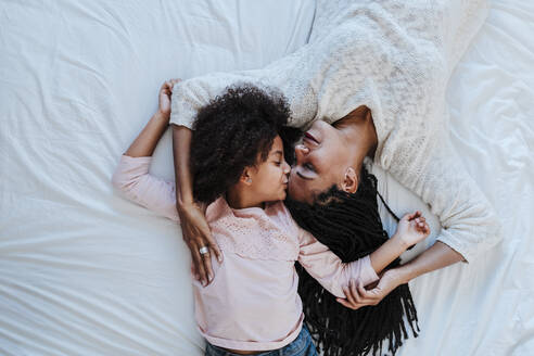 High angle view of daughter kissing mother while lying on bed at home - EBBF00942