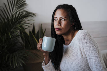 Reife Frau trinkt Kaffee, während sie zu Hause sitzt - EBBF00955