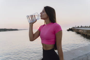 Woman drinking water while standing against sea - AFVF07364