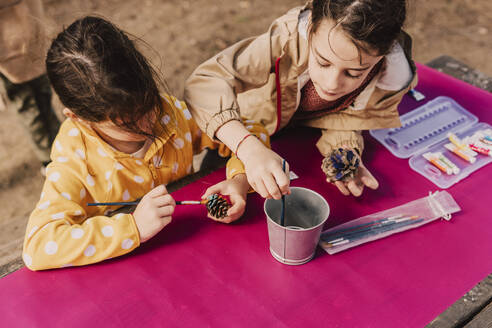 Sisters coloring pine cones at picnic table in park - ERRF04598