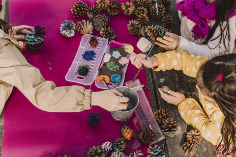 Girls decorating pine cones while coloring at picnic table in park stock photo