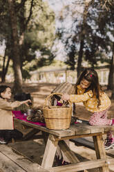 Girl collecting pine cone in wicker baskets at picnic table - ERRF04631