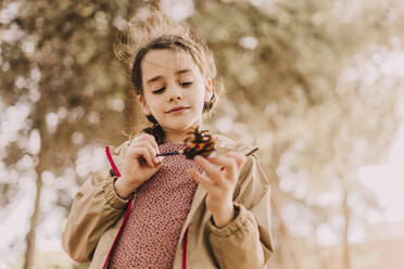 Cute girl coloring pine cone with paintbrush at park - ERRF04640