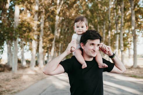Lächelnder Vater, der einen kleinen Jungen auf der Schulter trägt, während er im Freien steht - EBBF00976