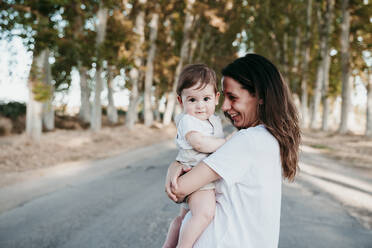 Smiling mother carrying baby boy while standing outdoors - EBBF00978