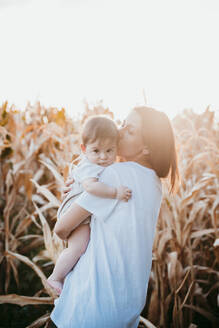 Mutter küsst kleinen Jungen, während sie bei Sonnenuntergang auf einem Feld steht - EBBF00983
