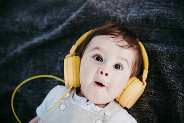 Niedlicher kleiner Junge mit Kopfhörern, der einen Gesichtsausdruck macht, während er auf einer Decke im Freien liegt - EBBF00988