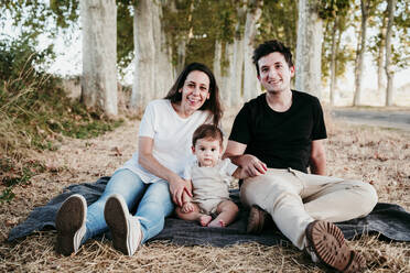 Smiling man and woman sitting with baby boy on blanket outdoors - EBBF00990