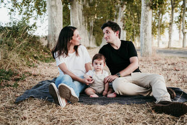 Couple talking while sitting with baby boy on blanket outdoors - EBBF00991