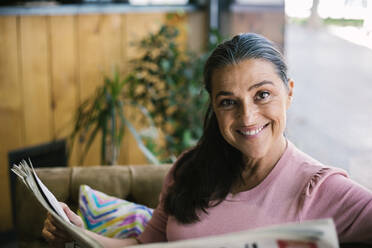 Smiling woman reading newspaper while sitting at cafe - XLGF00653