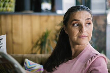 Thoughtful mature woman reading newspaper while sitting at cafe - XLGF00654