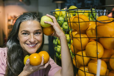 Lächelnde Frau mit frischem Obst in einem Metallkorb in einem Cafe - XLGF00658