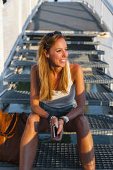 Lächelnde Frau schaut weg, während sie auf einer Treppe im Park sitzt - JMPF00483