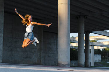 Smiling woman with arms outstretched enjoying while jumping at car park - JMPF00486