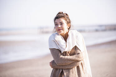 Beautiful young woman with arms crossed standing at beach against sky on sunny day - UUF21744