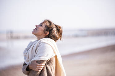 Lächelnde Frau mit verschränkten Armen und Blick auf den Strand an einem sonnigen Tag - UUF21745