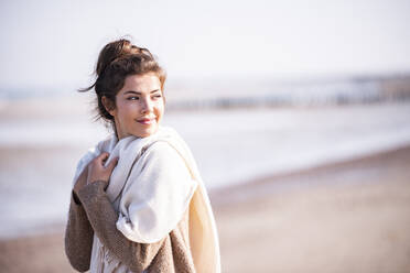 Thoughtful beautiful woman looking away while standing at beach on sunny day - UUF21746