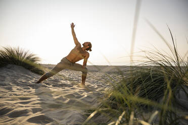 Shirtless junger Mann übt Dreieck Position Yoga am Strand gegen klaren Himmel während des Sonnenuntergangs - UUF21792
