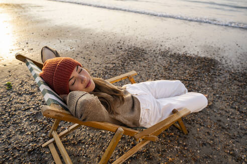 Young woman relaxing on folding chair at beach during sunset - UUF21809
