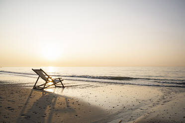 Empty folding chair on shore at beach against clear sky during sunset - UUF21817