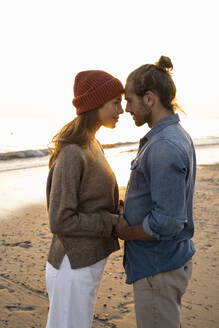 Junges romantisches Paar, das sich bei Sonnenuntergang am Ufer stehend ansieht - UUF21834